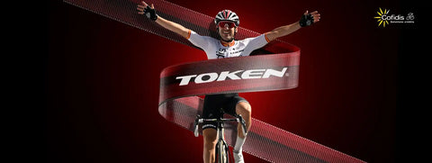 Syklister med armene hevet bak en ’TOKEN’-banner.